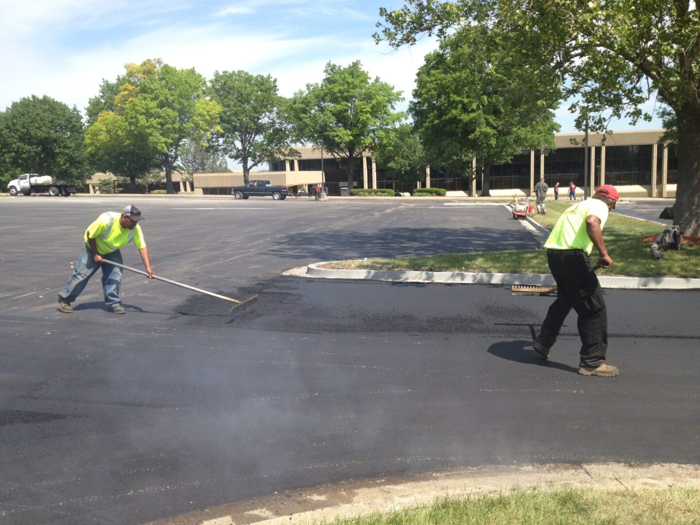 Two men in yellow shirts and one man is spraying water on asphalt.